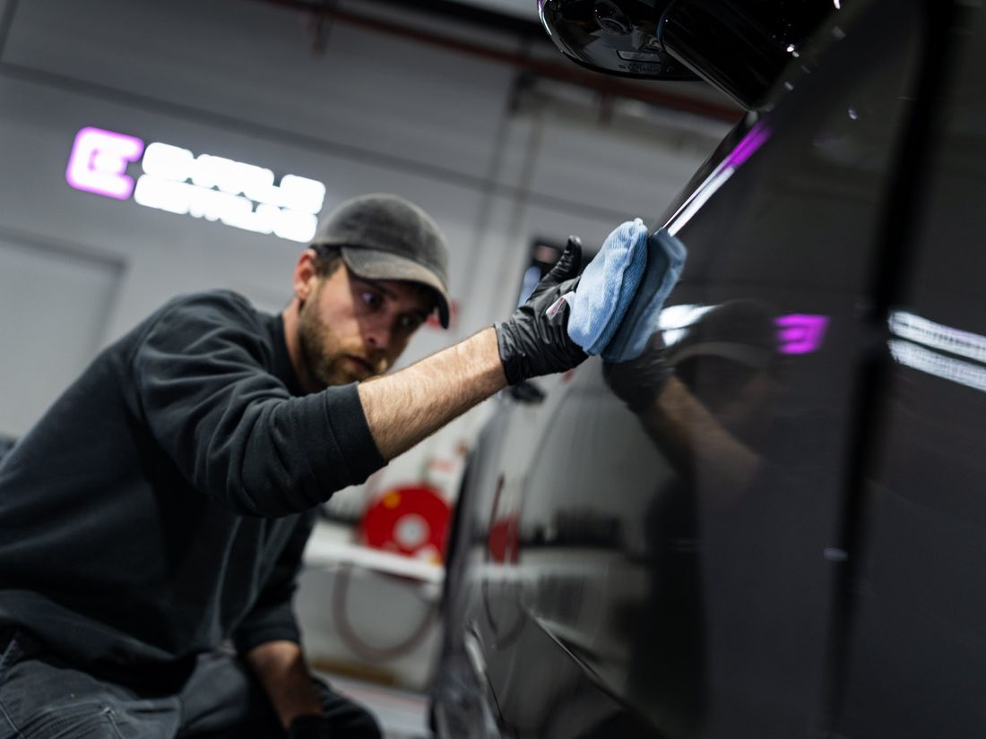 Medewerker van Charlie Detailing werkt een zwarte auto af